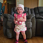 Mia joined the competition — help win amazing prizes! toddler, child, smiling, standing, hat, pink_clothing, sneakers, indoor, recliner, living_room, wood_floor, person, happy, cute, fashion, portrait, home, furniture, baby, casual