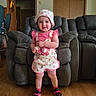 toddler, child, smiling, standing, hat, pink_clothing, sneakers, indoor, recliner, living_room, wood_floor, person, happy, cute, fashion, portrait, home, furniture, baby, casual