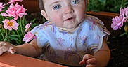 Mia is registered to the contest to win money with this photo: baby, child, flower_bed, pink_flowers, greenery, plant_pot, outdoor, nature, curious, portrait, infant, garden, cute, flora, young_child, face, hands, soft_lighting, colorful, happy