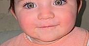 Mia is registered to the contest to win money with this photo: baby, child, face, smile, bib, food, snack, closeup, indoor, person, cute, young, happy, infant, apparel, holding, pattern, background, skin, eyelashes