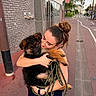 Rocky participe au concours pour gagner de l'argent avec cette photo : woman, puppy, dog, embracing, sidewalk, urban, smile, leash, building, street, casual_clothing, walking, happy, outdoor, daylight, hair_bun, black_dog, brown_dog, affection, pet