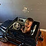 Nyairr is registered to the contest to win money with this photo: black_car, child, curious, face, floor, footwear, hands, indoor, looking_up, person, sandal, scuff_mark, seat, shirtless, steering_wheel, toddler, toy_car, vehicle, wall, wooden_floor