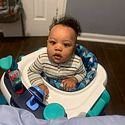 Nyairr is registered to the contest to win money with this photo: baby, child, infant, walker, toy, indoor, floor, striped_clothing, curly_hair, looking_up, expression, hands, seat, colorful, play, wooden_floor, home, person, young, cute