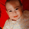 adorable, baby, baby_garment, child, closeup, clothing, cute, face, happy, indoor, infant, lying_down, person, polka_dot, portrait, red_background, smiling, soft_light, warm_color, young