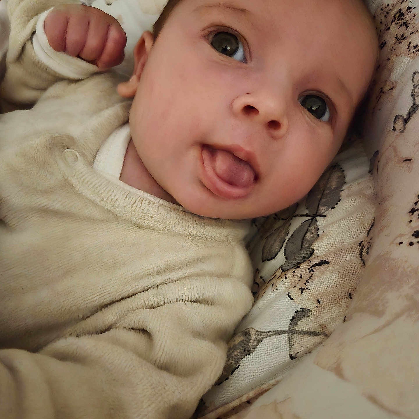 Yuna a rejoint le concours — aidez-le/la à gagner de superbes lots ! baby, infant, face, tongue_out, hand, fist, clothing, cream_color, cushion, pattern, closeup, portrait, cute, child, soft_texture, lying_down, indoors, expression, young_child, person