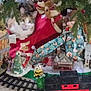 cat, christmas_tree, holiday_decor, stuffed_animal, toy_train, train_track, figurine, miniature_building, red_blanket, greenery, indoor, festive, decorations, plush_toy, animal, pet, christmas, holiday, cozy, curious