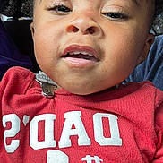 Derrell is registered to the contest to win money with this photo: child, toddler, face, curly_hair, red_shirt, text_on_clothing, close_up, portrait, expression, casual, indoors, cute, young_child, person, fashion, clothing, skin, head, eyes, mouth