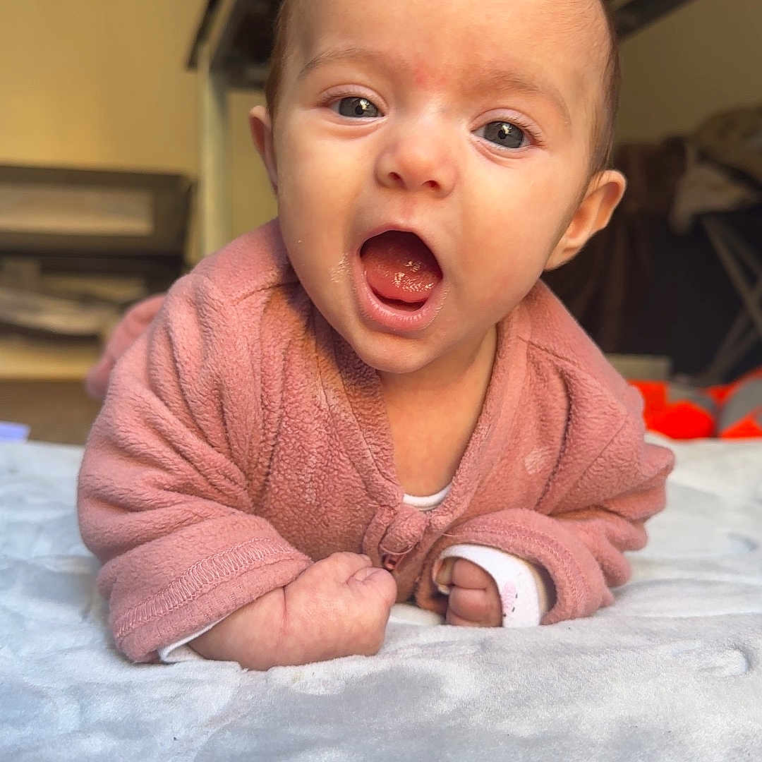 Alizée participe au concours pour gagner de l'argent avec cette photo : baby, bed, blanket, child, cozy, cute, expression, eyebrows, face, head, human, indoor, infant, lying_down, mouth_open, person, pink_clothing, skin, soft_texture, young_child