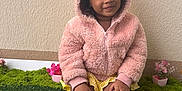 Jade a rejoint le concours — aidez-le/la à gagner de superbes lots ! child, toddler, pink_hoodie, yellow_shorts, slippers, bunny_slippers, smiling, sitting, green_grass, artificial_grass, potted_plants, flowers, indoor, cute, happy, portrait, cozy_clothing, wall, hands, feet