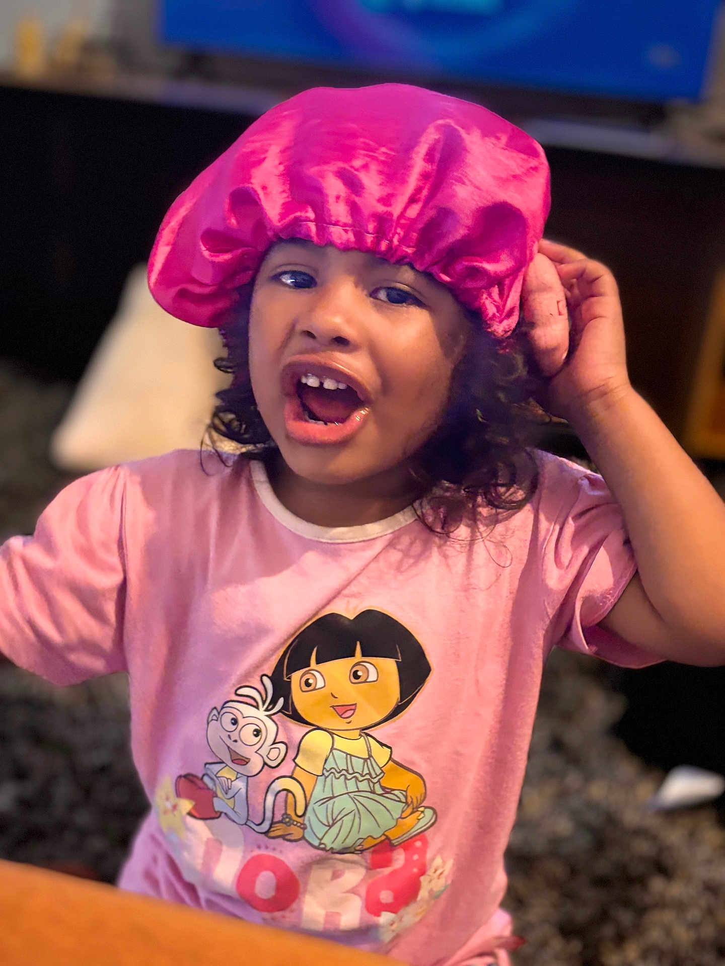 Jade a rejoint le concours — aidez-le/la à gagner de superbes lots ! child, pink_bonnet, dora_the_explorer, tshirt, indoor, curly_hair, expression, person, cartoon_character, table, carpet, furniture, portrait, young_child, clothing, cute, animated, home, smiling, talking