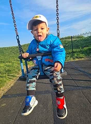 Andrei is registered to the contest to win money with this photo: arm, asphalt, baby, cloud, electric_blue, eye, fun, happy, human_body, knee, outdoor_play_equipment, person, plant, playground, recreation, shoe, sky, smile, sneakers, swing