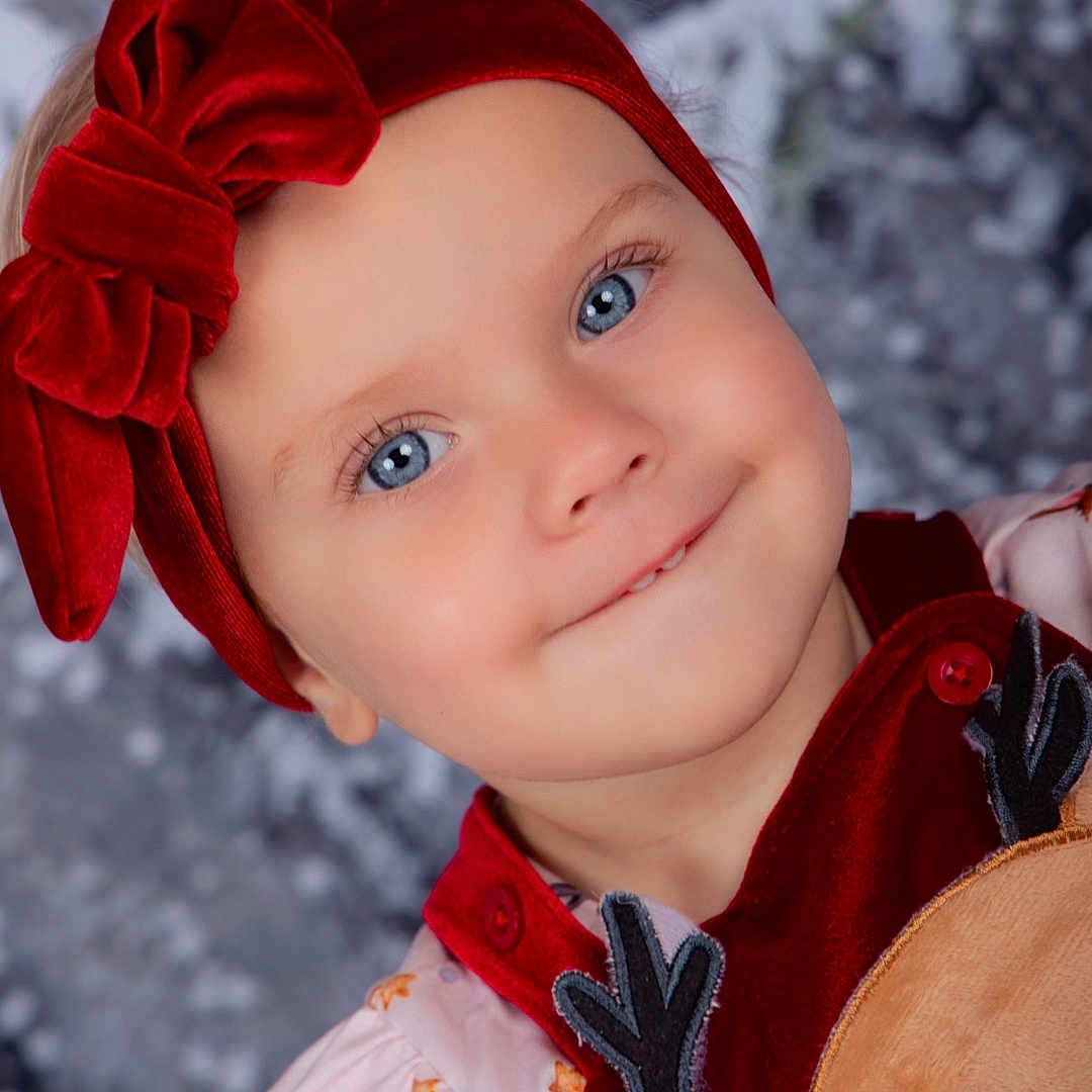 Raven is registered to the contest to win money with this photo: baby, blue_eyes, button, child, close_up, cute, face, festive, happy, holiday_clothing, innocent, pink_dress, portrait, red_headband, reindeer, smiling, toddler, velvet_bow, winter_background, young_child