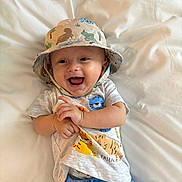 Forrest is registered to the contest to win money with this photo: baby, infant, smiling, hat, bucket_hat, tshirt, animal_print, blue_pants, lying_down, happy, child, cute, indoors, white_background, clapping_hands, playful, young, casual_clothing, portrait, joyful
