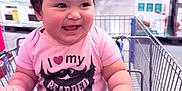 Amelia is registered to the contest to win money with this photo: baby, child, shopping_cart, store, aisle, pink, hair_ties, shirt, cute, happy, smile, chubby, clothing, retail, indoor, person, holding, funny_shirt, sitting, shopping