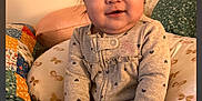 Amelia is registered to the contest to win money with this photo: baby, child, indoor, pillow, bed, blanket, clothing, cute, person, smiling, seated, infant, soft_toys, patterned, warm, cozy, portrait, head, hands, footwear
