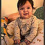 Amelia is registered to the contest to win money with this photo: baby, child, indoor, pillow, bed, blanket, clothing, cute, person, smiling, seated, infant, soft_toys, patterned, warm, cozy, portrait, head, hands, footwear