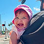 baby, child, pink_hat, smiling, tattoo, adult, black_shirt, outdoor, sunny, daylight, traffic_light, street, crosswalk, blue_sky, happy, person, holding, arm, face, summer
