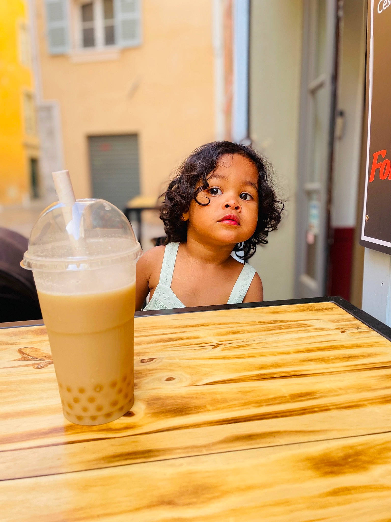 Malika participe au concours pour gagner de l'argent avec cette photo : cup, drink, drinking, drinking_straw, drinkware, flooring, food, hardwood, ingredient, juice, non_alcoholic_beverage, person, soft_drink, table, tableware, toddler, varnish, window, wood, wood_stain