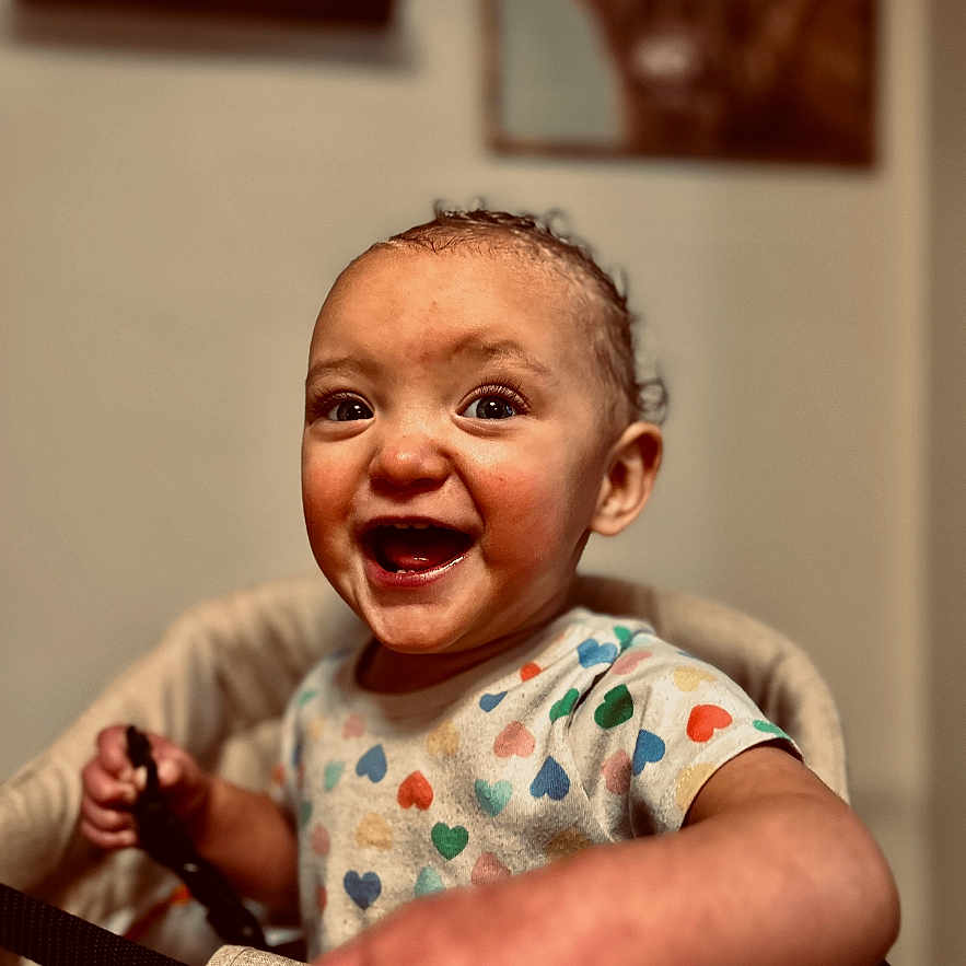 Journey joined the competition — help win amazing prizes! baby, child, curly_hair, cute, face, hand, happy, heart_pattern, high_chair, holding, home, indoor, painting, person, seat, shirt, smiling, toddler, wall_art, wooden_table