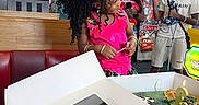 Baby Doll is registered to the contest to win money with this photo: child, birthday, cake, party, pink_outfit, curly_hair, hair_bow, tiara, arcade, restaurant, indoor, people, smiling, celebration, gift_box, birthday_candle, friend, seated, colorful, photograph