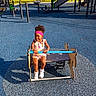 child, toddler, girl, smiling, playground, playground_equipment, spring_ride, outdoor, park, play_area, sunlight, trees, rubber_surface, colorful, dress, headband, curly_hair, sneakers, portrait, recreation