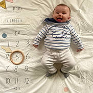 Mylann participe au concours pour gagner de l'argent avec cette photo : arrow, baby, child, clothing, decorations, face, floor, happy, infant, lying_down, milestone_blanket, months, numbers, pants, portrait, smiling, socks, striped_shirt, tongue_out, wooden_ring