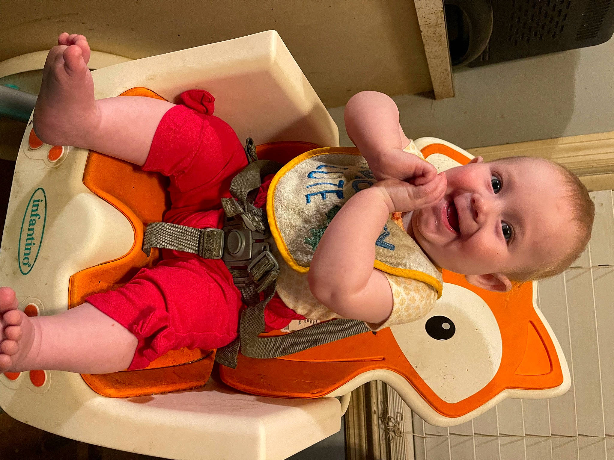 Scarlett is registered to the contest to win money with this photo: arm, baby, baby_laughing, baby_products, baby_toddler_clothing, child, comfort, finger, fun, happy, knee, mouth, orange, person, red, room, smile, t_shirt, thigh, thumb