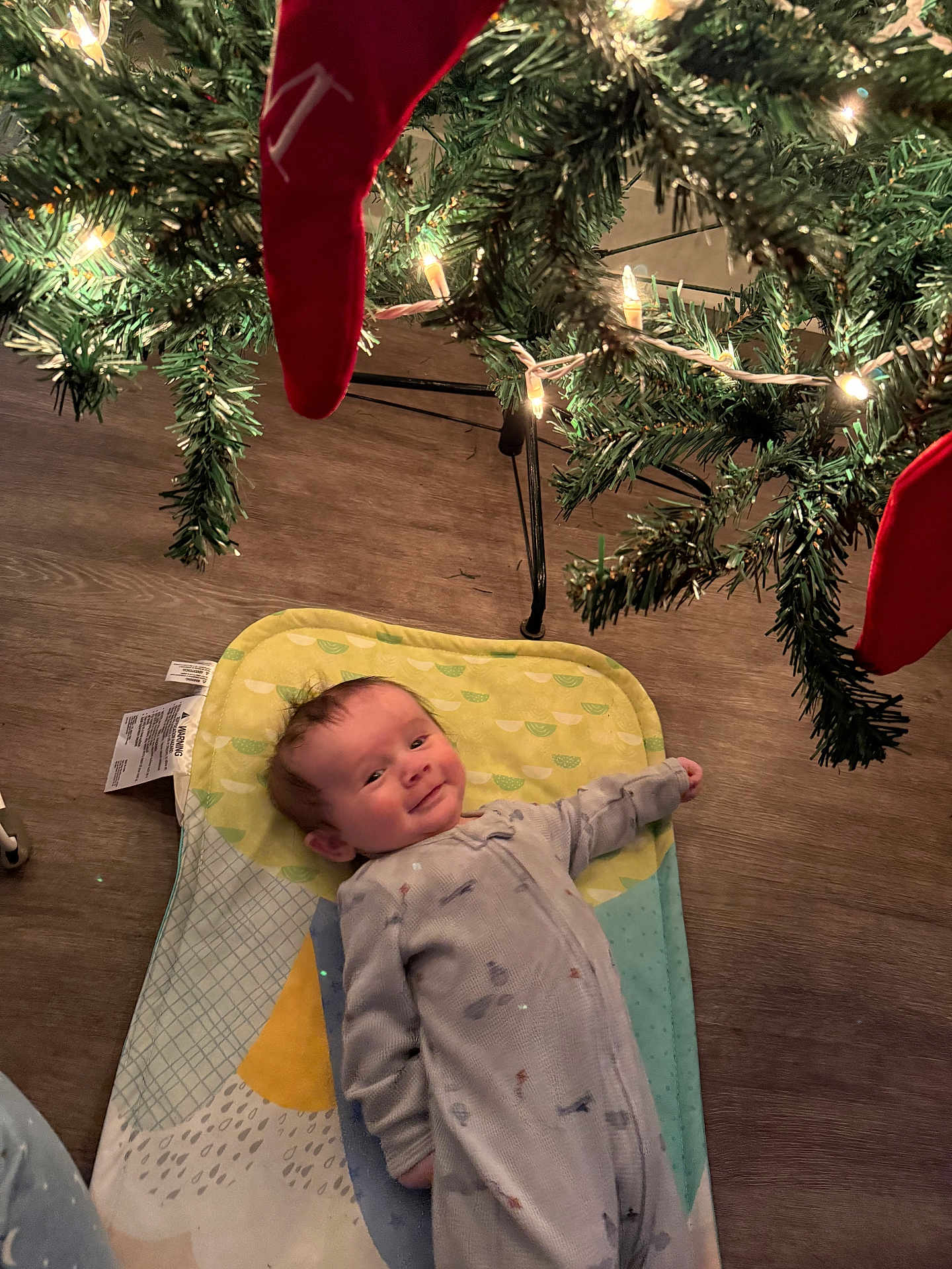 John joined the competition — help win amazing prizes! baby, infant, christmas_tree, christmas_lights, red_stocking, floor, pajamas, mat, holiday, smile, indoors, wood_floor, festive, child, decoration, greenery, cozy, cute, lying_down, celebration
