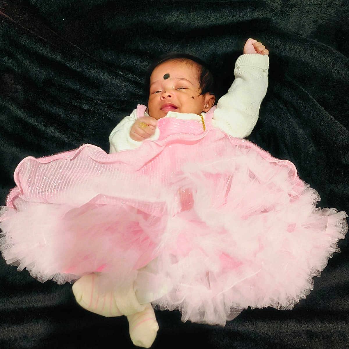 Leïa Thikshitha participe au concours pour gagner de l'argent avec cette photo : adorable, baby, black_blanket, child, cozy, cute, face, footwear, head, indoors, infant, legs, lying_down, one_arm_up, pink_dress, portrait, sleepy, small, soft_texture, white_sweater