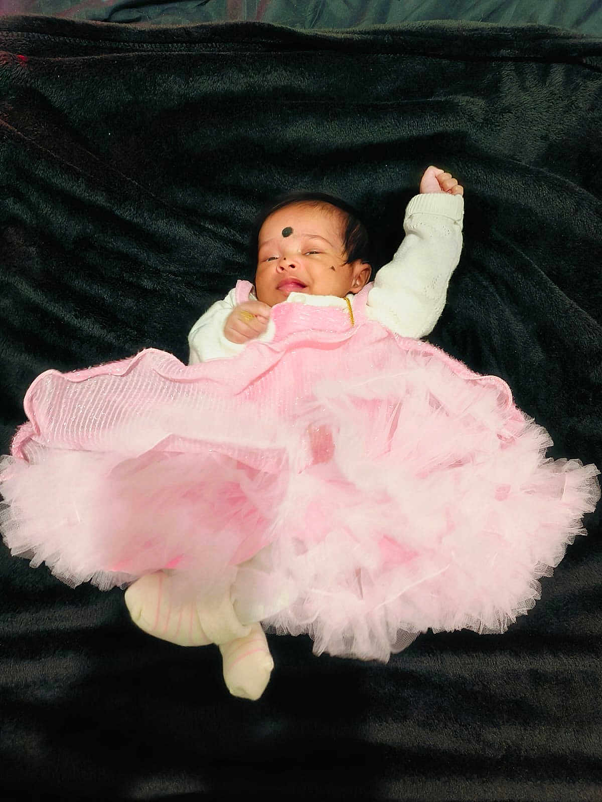 Leïa Thikshitha participe au concours pour gagner de l'argent avec cette photo : adorable, baby, black_blanket, child, cozy, cute, face, footwear, head, indoors, infant, legs, lying_down, one_arm_up, pink_dress, portrait, sleepy, small, soft_texture, white_sweater