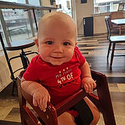 Graesyn is registered to the contest to win money with this photo: baby, child, high_chair, red_shirt, smiling, indoors, cafe, wooden_furniture, natural_light, window, flooring, person, cute, happy, infant, seat, hand, face, head, foot