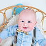 baby, child, smile, blue_eyes, bow_tie, suspenders, light_blue_shirt, beige_pants, wicker_chair, fluffy_cushion, indoor, portrait, happy, cute, infant, seated, pastel_background, closeup, plush, fashion