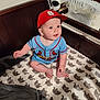 Graesyn is registered to the contest to win money with this photo: baby, baseball_cap, blanket, blue_jersey, cat_pattern, child, clothing, crib, cute, diapers, happy, indoors, infant, person, red_cap, sheet, sitting, smiling, wooden_crib, young_child