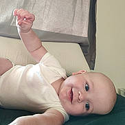 Graesyn joined the competition — help win amazing prizes! baby, infant, smile, face, arm, hand, blanket, bed, couch, curtain, indoor, person, child, happy, skin, clothing, reaching, lying_down, blue_eyes, head
