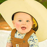 Graesyn joined the competition — help win amazing prizes! baby, background_blur, child, closeup, clothing, cowboy_hat, cute, expression, face, happy, headwear, infant, nature, outdoor, overalls, person, portrait, smiling, sunlight, young