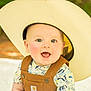 baby, background_blur, child, closeup, clothing, cowboy_hat, cute, expression, face, happy, headwear, infant, nature, outdoor, overalls, person, portrait, smiling, sunlight, young