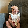 baby, child, smile, headband, pink_bow, striped_outfit, chair, gray_chair, plush, happy, tongue_out, cute, indoor, person, infant, sitting, wooden_sign, skin, face, young_child