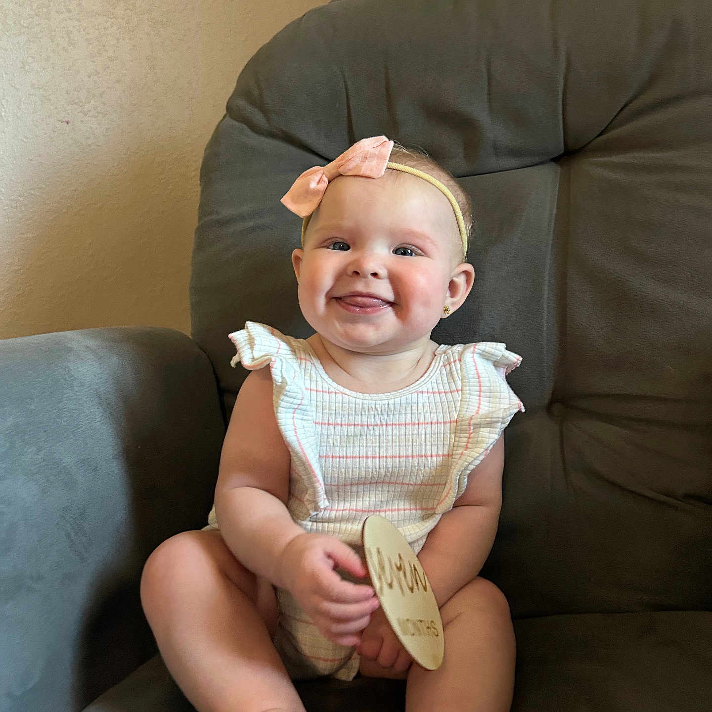 Mayci joined the competition — help win amazing prizes! baby, child, smile, headband, pink_bow, striped_outfit, chair, gray_chair, plush, happy, tongue_out, cute, indoor, person, infant, sitting, wooden_sign, skin, face, young_child