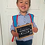 child, smile, backpack, chalkboard, door, blue_shirt, jeans, first_day, kindergarten, happy, indoors, standing, boy, short_hair, casual_clothing, portrait, education, school, sign, announcement