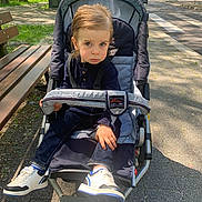 David participe au concours pour gagner de l'argent avec cette photo : bench, casual, child, clothing, daylight, expression, nature, outdoor, park, pavement, person, seat, shoes, sidewalk, stroller, sunlight, toddler, trees, urban, young_child