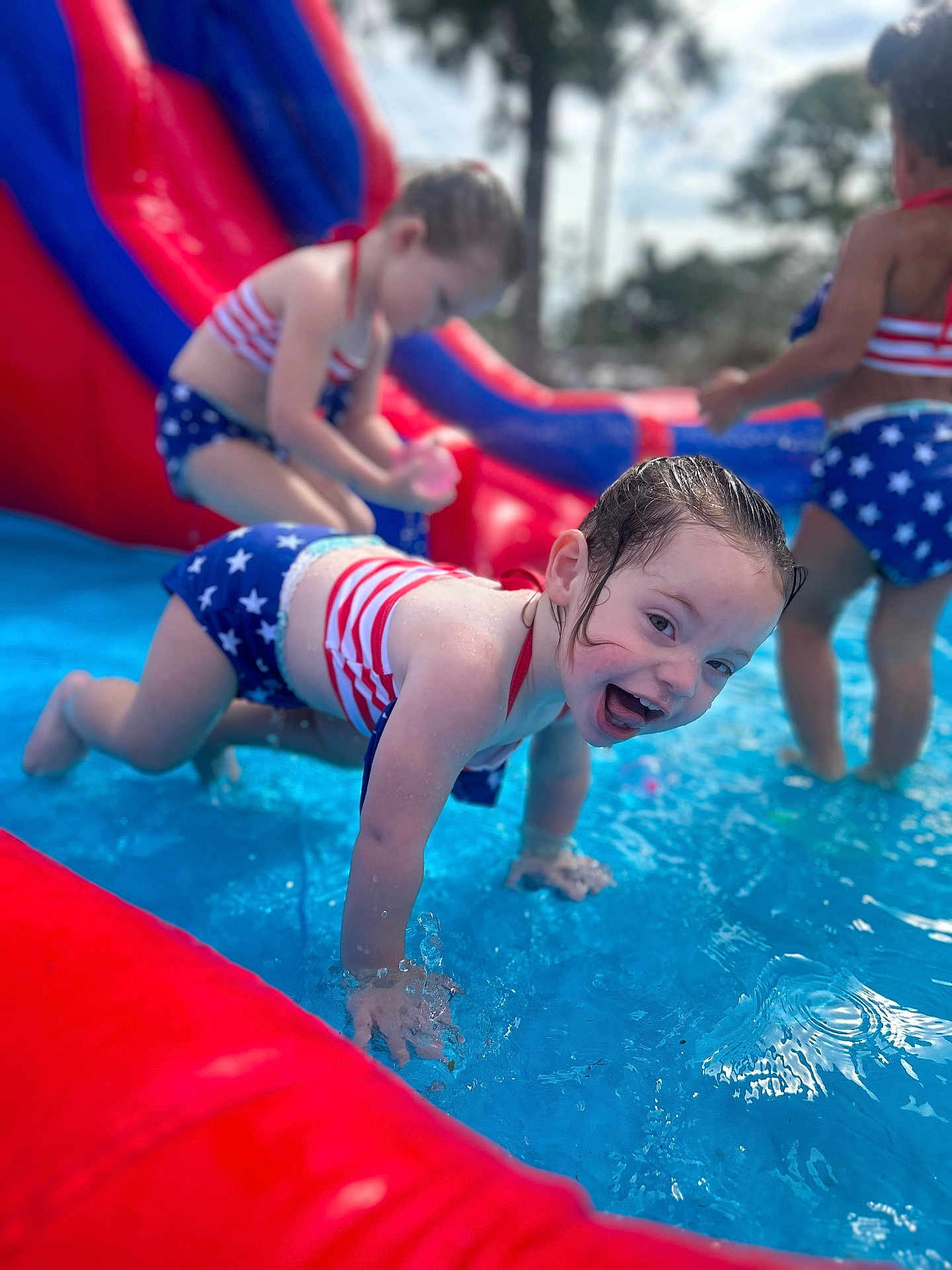 Lilyana joined the competition — help win amazing prizes! child, children, swimsuit, inflatable_pool, water, splashing, playing, summer, outdoor, slide, red, blue, star_pattern, happy, crawling, fun, pool, sunny, smiling, person