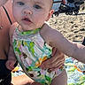 baby, child, infant, swimsuit, floral_pattern, beach, sand, stroller, adult_hand, outdoor, sunlight, blanket, summer, cute, person, portrait, closeup, skin, expression, vacation