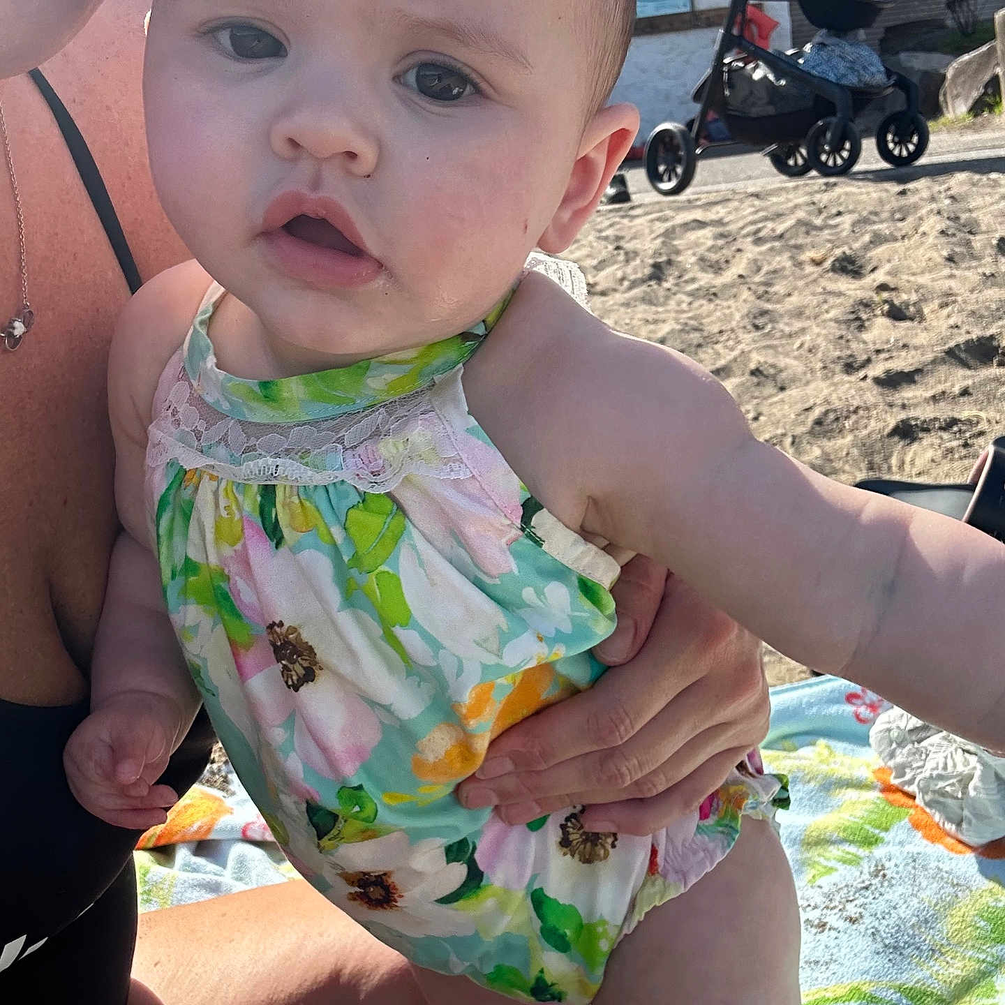 Addison joined the competition — help win amazing prizes! baby, child, infant, swimsuit, floral_pattern, beach, sand, stroller, adult_hand, outdoor, sunlight, blanket, summer, cute, person, portrait, closeup, skin, expression, vacation