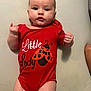 baby, bodysuit, child, clothing, cute, expression, face, hands, human, indoor, infant, ladybug, looking, lying_down, person, portrait, red_onesie, skin, small_fingers, young