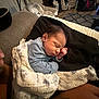 baby, newborn, sleeping, blanket, cushion, pillow, infant, indoor, person, tattoo, hand, furniture, living_room, stroller, basket, floor, carpet, soft_lighting, cozy, rest