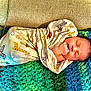 Eli joined the competition — help win amazing prizes! baby, newborn, swaddle, blanket, couch, infant, sleeping, face, hand, animal_print, cozy, colorful, texture, indoors, resting, child, soft, peaceful, portrait, wrapped