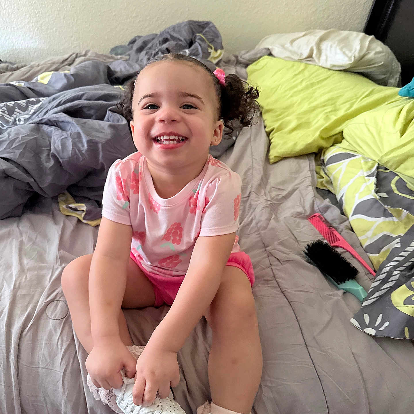 Jo'Mila King joined the competition — help win amazing prizes! bed, blanket, child, comb, curly_hair, cute, hairbrush, happy, indoors, messy_bed, person, pillow, pink_clothing, playful, room, sitting, smiling, toddler, white_shoes, young_child