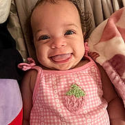 Dàmia is registered to the contest to win money with this photo: baby, child, smile, tongue_out, pink_clothing, bow, strawberry_patch, blanket, soft_fabric, cute, portrait, happy, infant, lying_down, indoors, face, head, cheerful, closeup, person