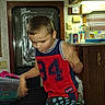 Michael is registered to the contest to win money with this photo: child, boy, toddler, indoor, portrait, sitting, leaning, shirt, jersey, red_clothing, blue_clothing, number_94, face, short_hair, kitchen, rv_interior, window, cabinets, bottles, sock
