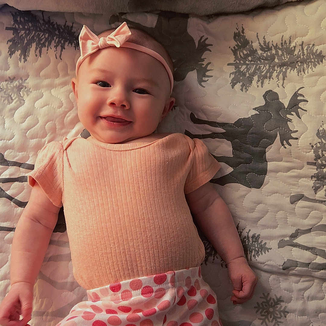 Jalynn is registered to the contest to win money with this photo: apparel, baby, bow, child, cute, happy, headband, indoors, infant, lying_down, peach_clothing, person, pink, polka_dot_pants, portrait, quilted_blanket, reindeer_pattern, smiling, snowflake_pattern, soft_lighting